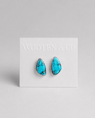 A pair of Wooten & Co stud earrings with turquoise blue marbled stones in silver bezel settings, mounted on a white display card against a light gray background.