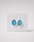 A pair of Wooten & Co turquoise stud earrings with a teardrop shape and silver settings, mounted on a white display card against a light gray background.