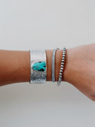 Wooten & Co. Stowell turquoise cuff bracelet in hammered sterling silver worn on a wrist with two other bracelets.