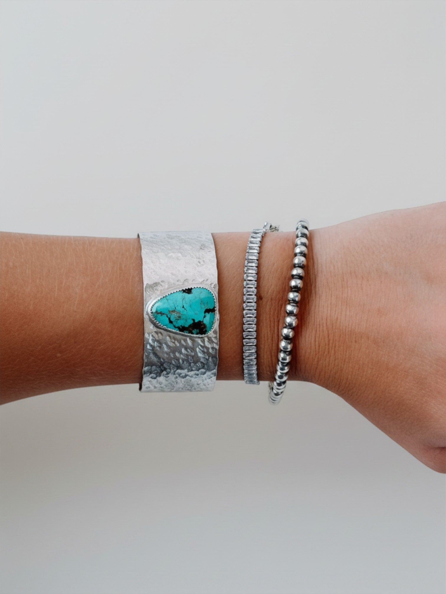 Wooten & Co. Stowell turquoise cuff bracelet in hammered sterling silver worn on a wrist with two other bracelets.